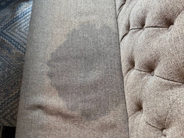 Upholstery before cleaning, showing a large visible stain and discoloration on a brown sofa cushion.