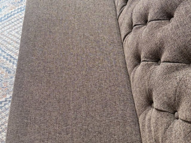 Close-up of a large, dark brown stain on a light-colored fabric sofa before upholstery cleaning services