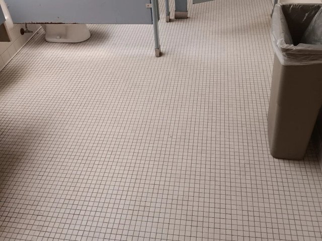 Grungy, stained white ceramic tile floor with dark, dirty grout lines before cleaning